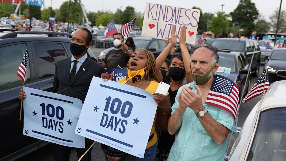 Biden supporters applaud and carry American flags, as well as placards saying 