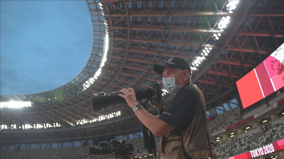 Photographer Bernard Brault wears a mask behind his camera.