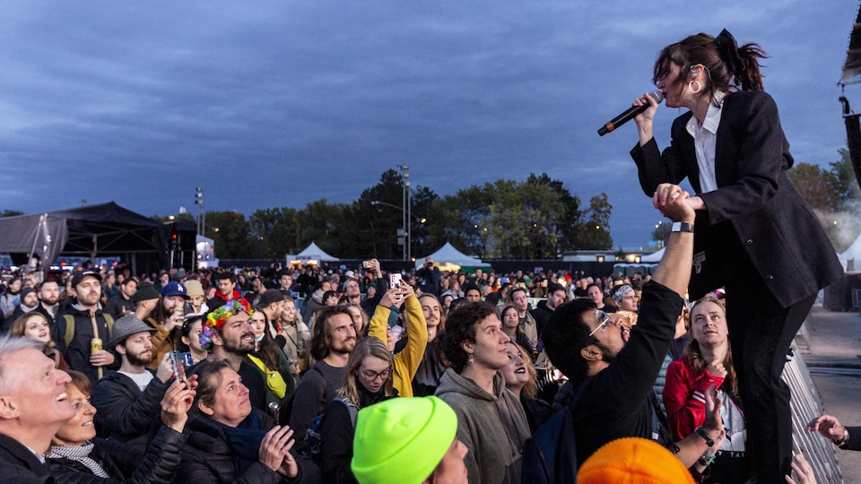 A singer balances on the fence in front of the stage and balances herself holding the spectator's hand.