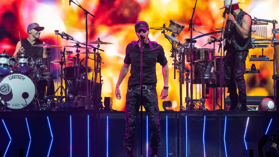 Enrique Iglesias singing behind a microphone on stage with musicians.