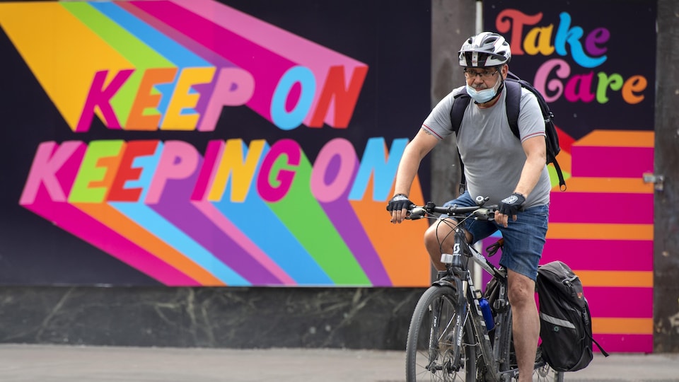 A man on a bicycle in front of a colorful mural in downtown Toronto.