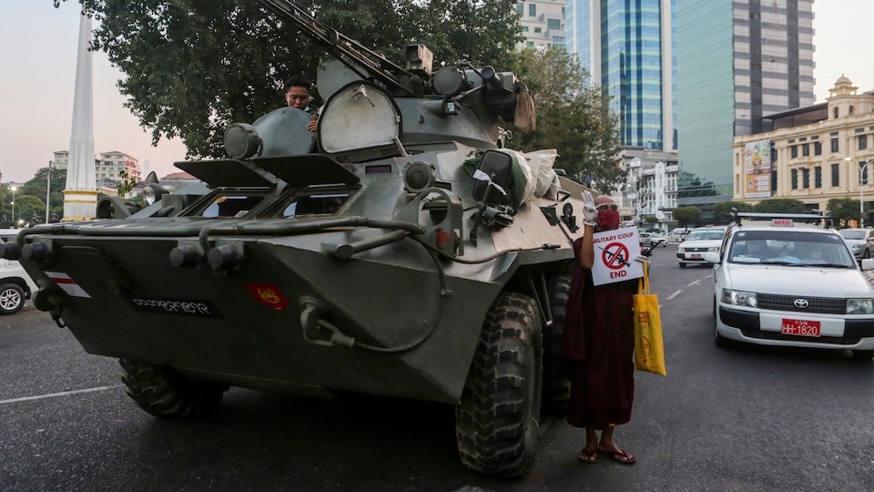 An armored tank is in the middle of the city center and a protester holds a sign calling for an end to the coup. 