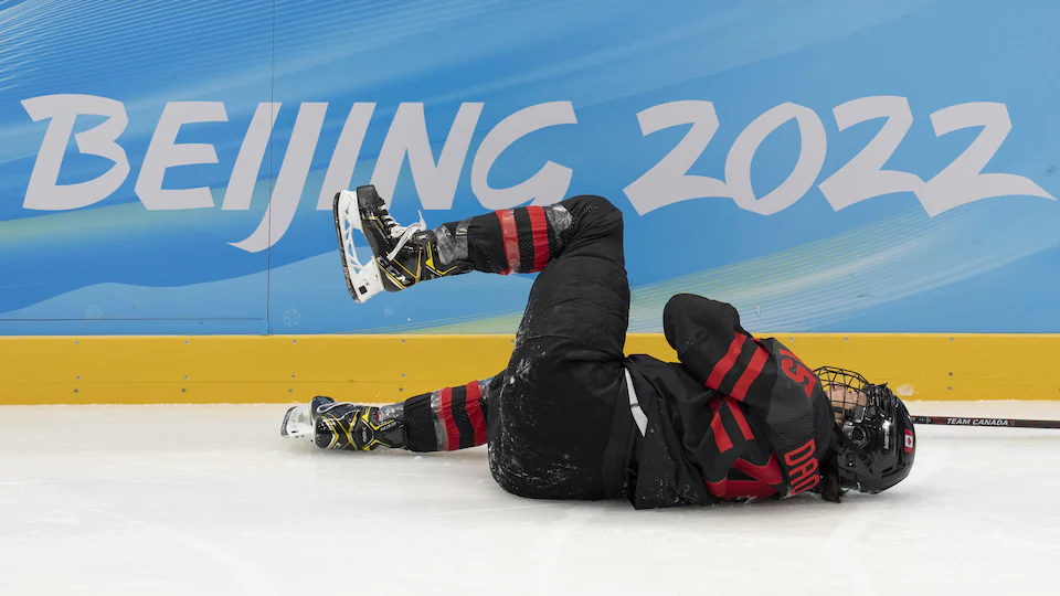 Hockey player lying on the ice holding her right shoulder.