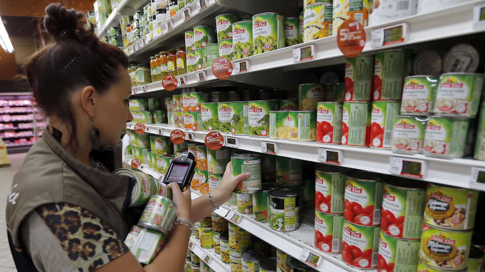 A supermarket worker studies various canned vegetables in front of her on a high screen display.