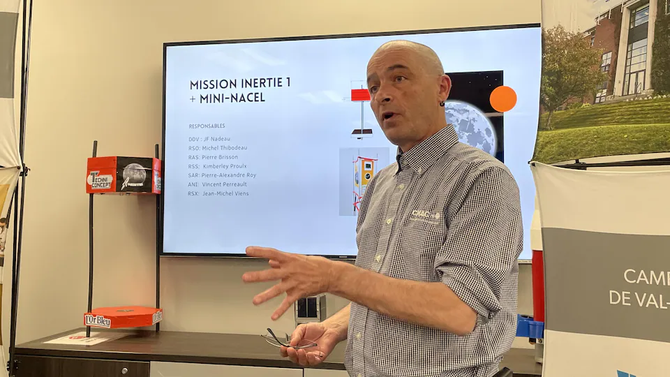 Jean Francois Nadeau in front of a TV on which a slide show is being presented.